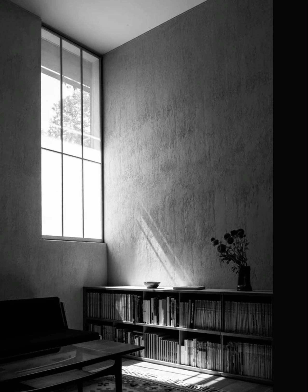 Luz de una ventana alta sobre un muro y un librero bajo.